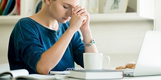 young woman praying while working on her computer