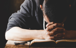 man praying with folded hands and head on bible